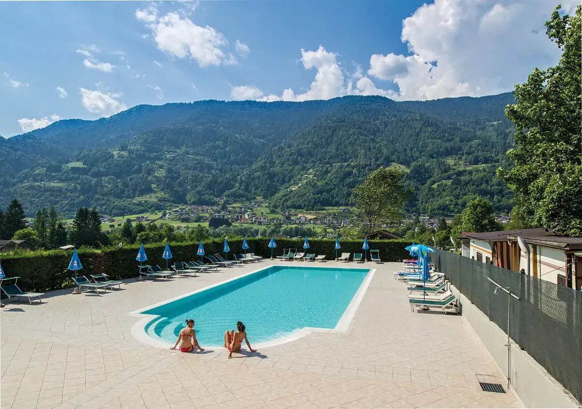 Due ragazze si rilassano a bordo piscina in un campeggio Calavise, con montagne verdi sullo sfondo.