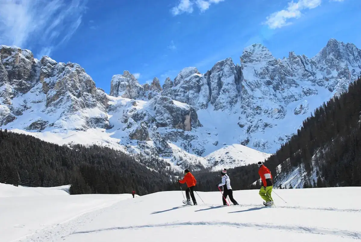 Persone in escursioni invernali in Trentino, con montagne innevate e cielo azzurro.