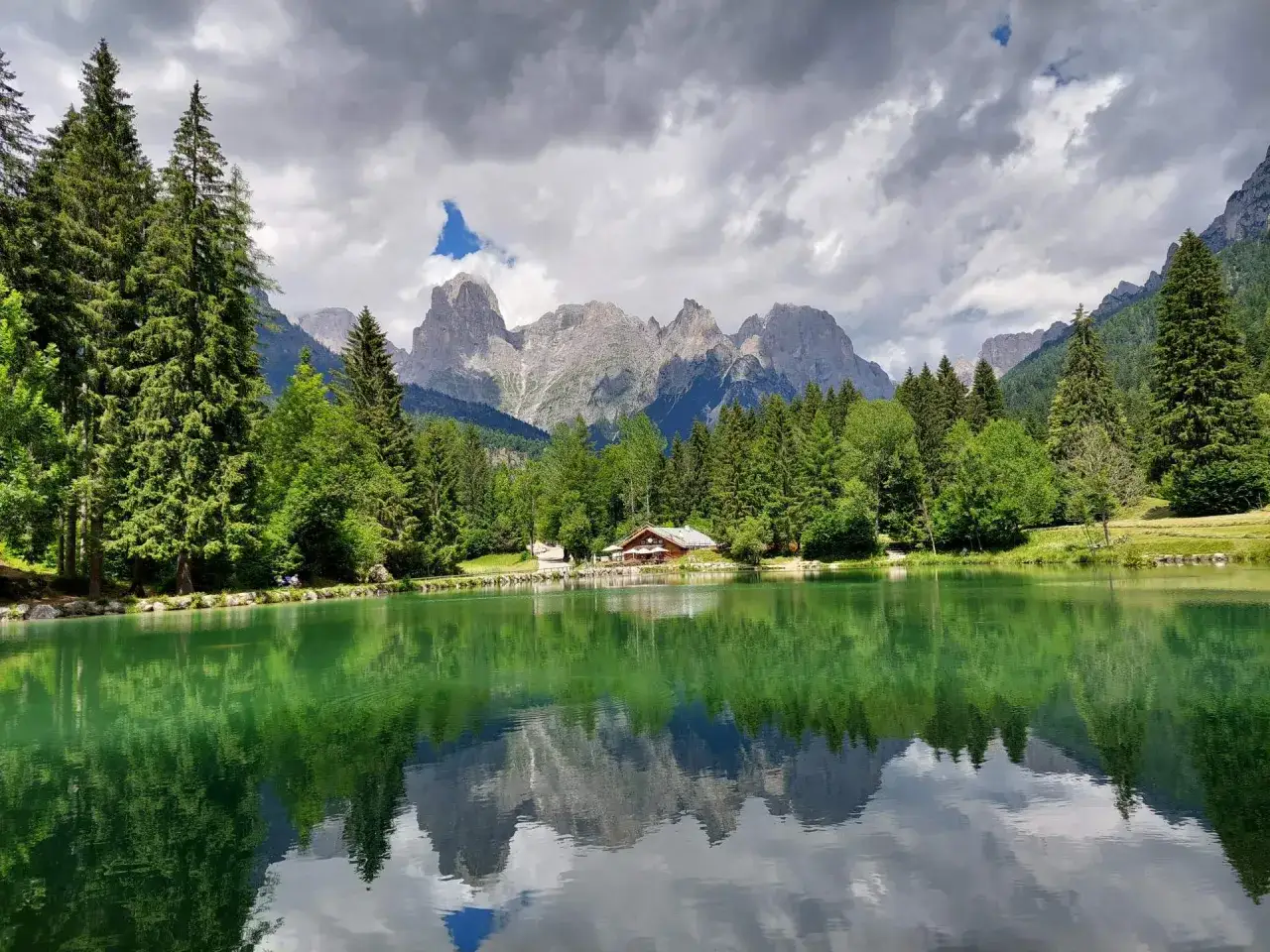 Riflessi perfetti sul lago Welsperg, con montagne maestose e un rifugio accogliente tra i pini.