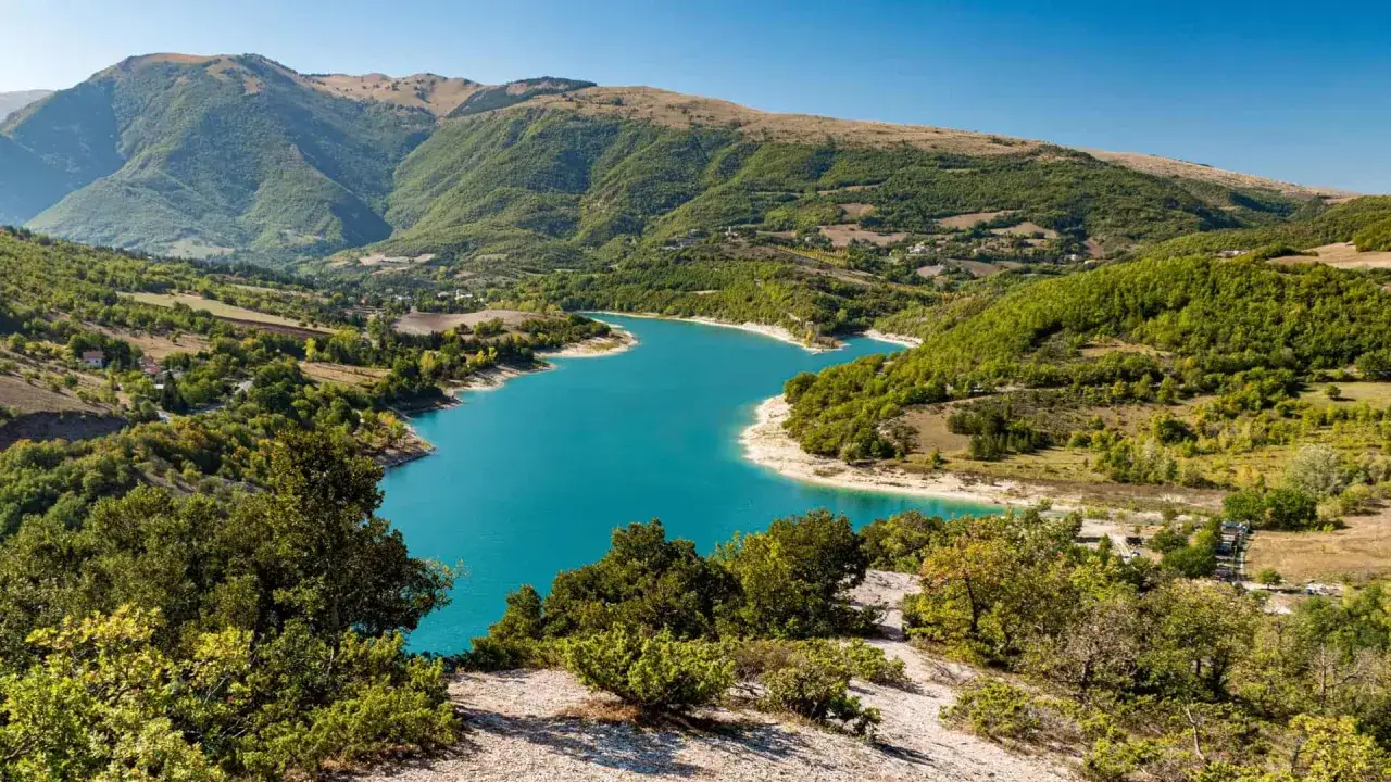 Il lago di Fiastra brilla di un azzurro intenso tra colline verdi e montagne maestose, un vero gioiello naturale.
