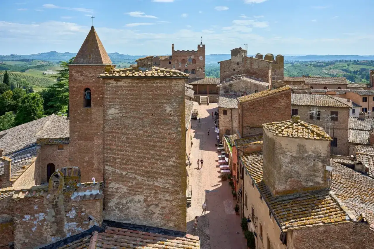 Vista dall'alto di Certaldo Alto, con il campanile di una chiesa in mattoni rossi, tetti in tegole e colline toscane sullo sfondo.