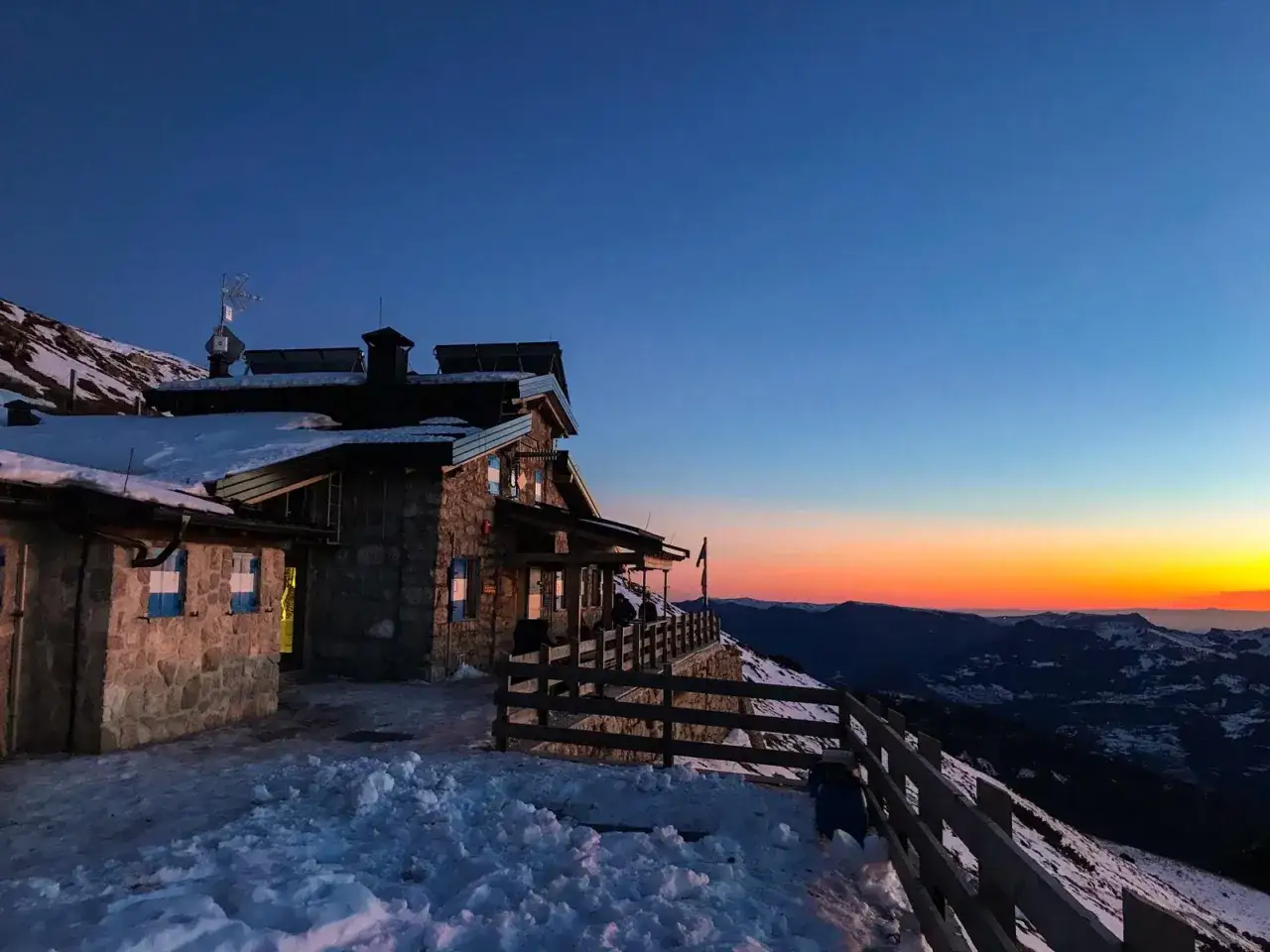 Rifugio sul Monte Stivo al tramonto, con neve e un cielo dai colori caldi.