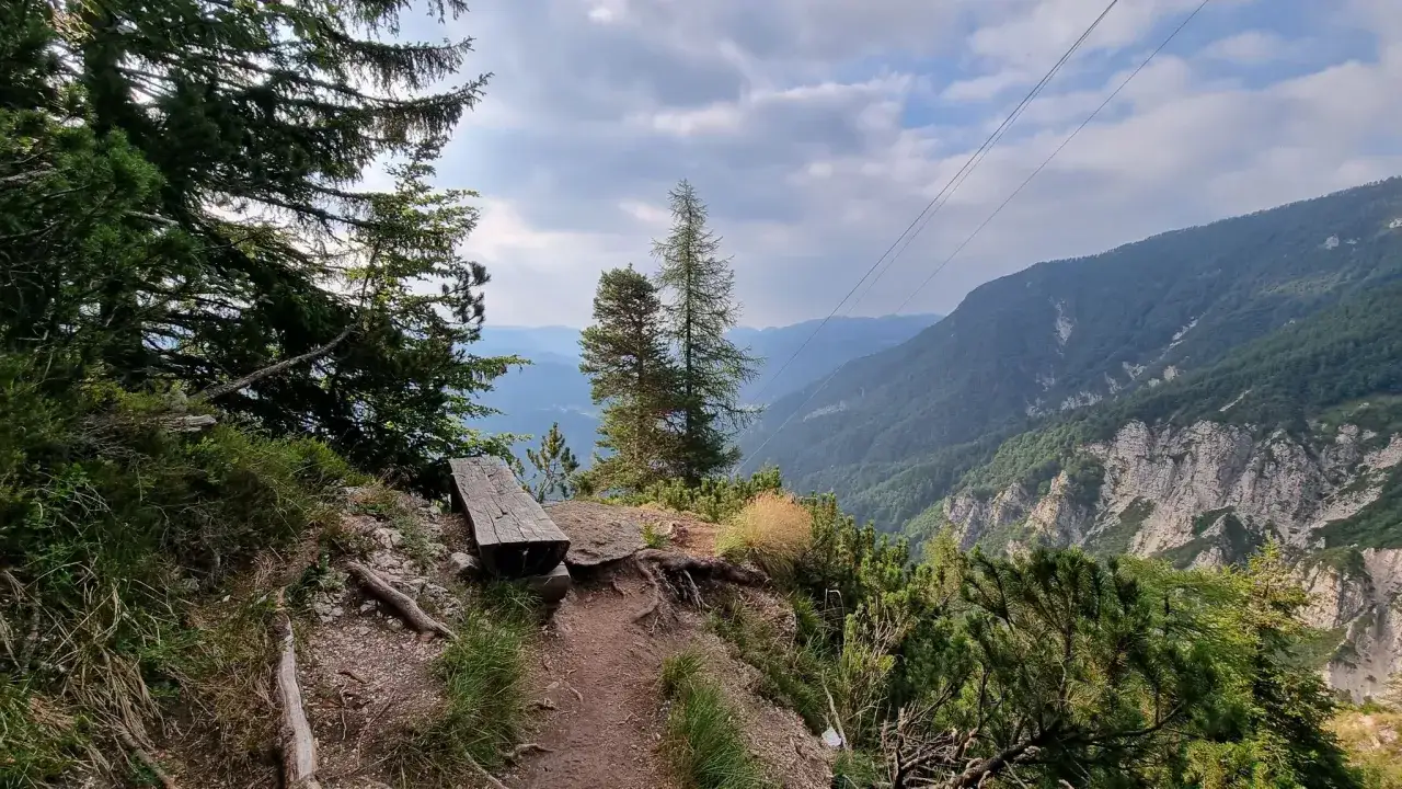 Sentiero panoramico con panchina in legno vicino al rifugio Casarota. Montagne verdi e cielo nuvoloso.