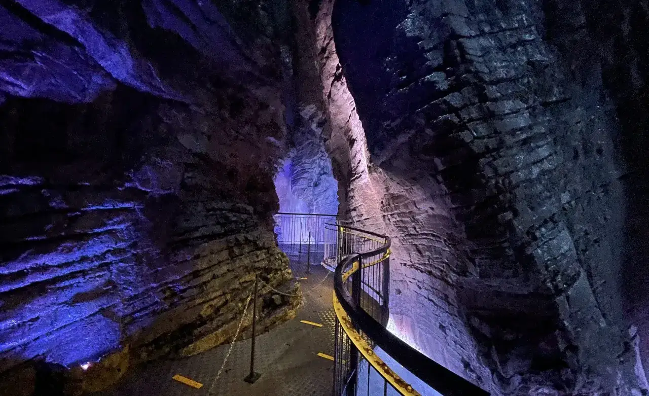 Sentiero illuminato da luci blu e viola tra le rocce delle Cascate del Varone. Un corrimano curvo guida i visitatori in questo suggestivo percorso.