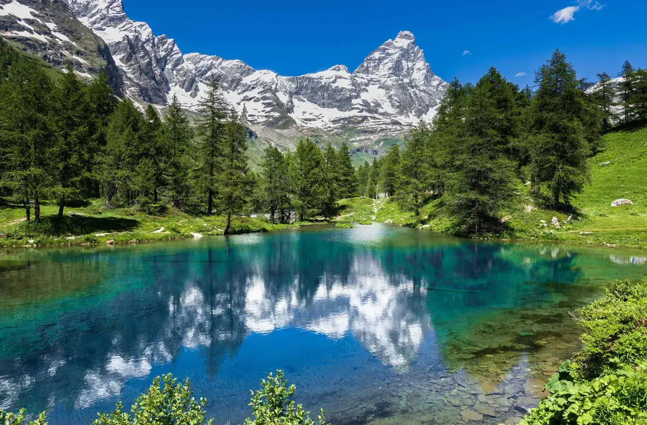 Lago alpino cristallino con riflessi montuosi e boschi verdi. Ideale per scoprire le cose da fare in estate.