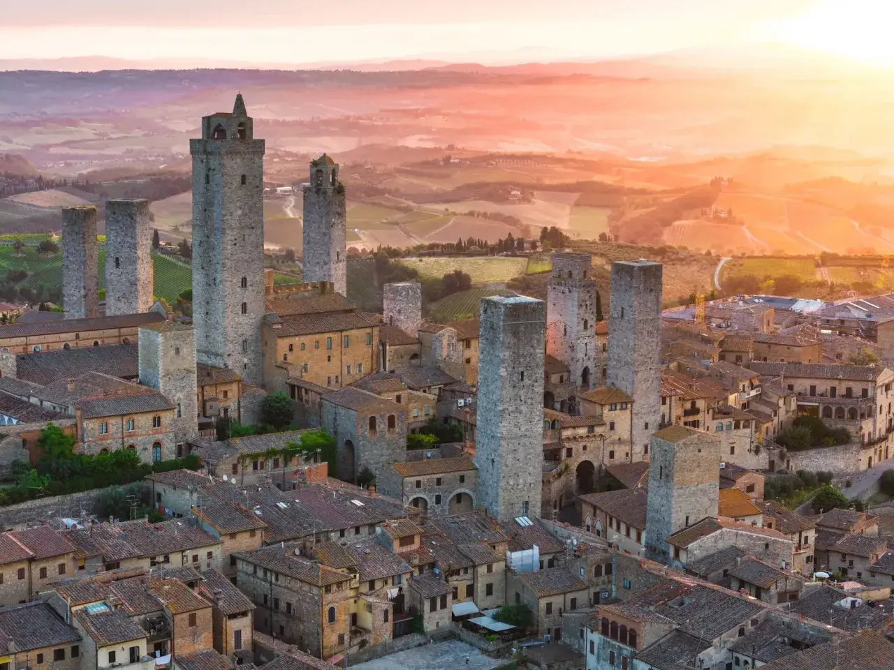 Torri medievali di San Gimignano si stagliano contro un tramonto dorato, con colline toscane sullo sfondo.
