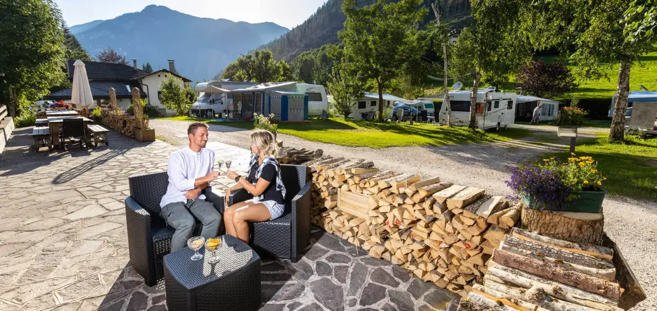 Coppia brinda al camping Valle Verde tra camper e montagne.