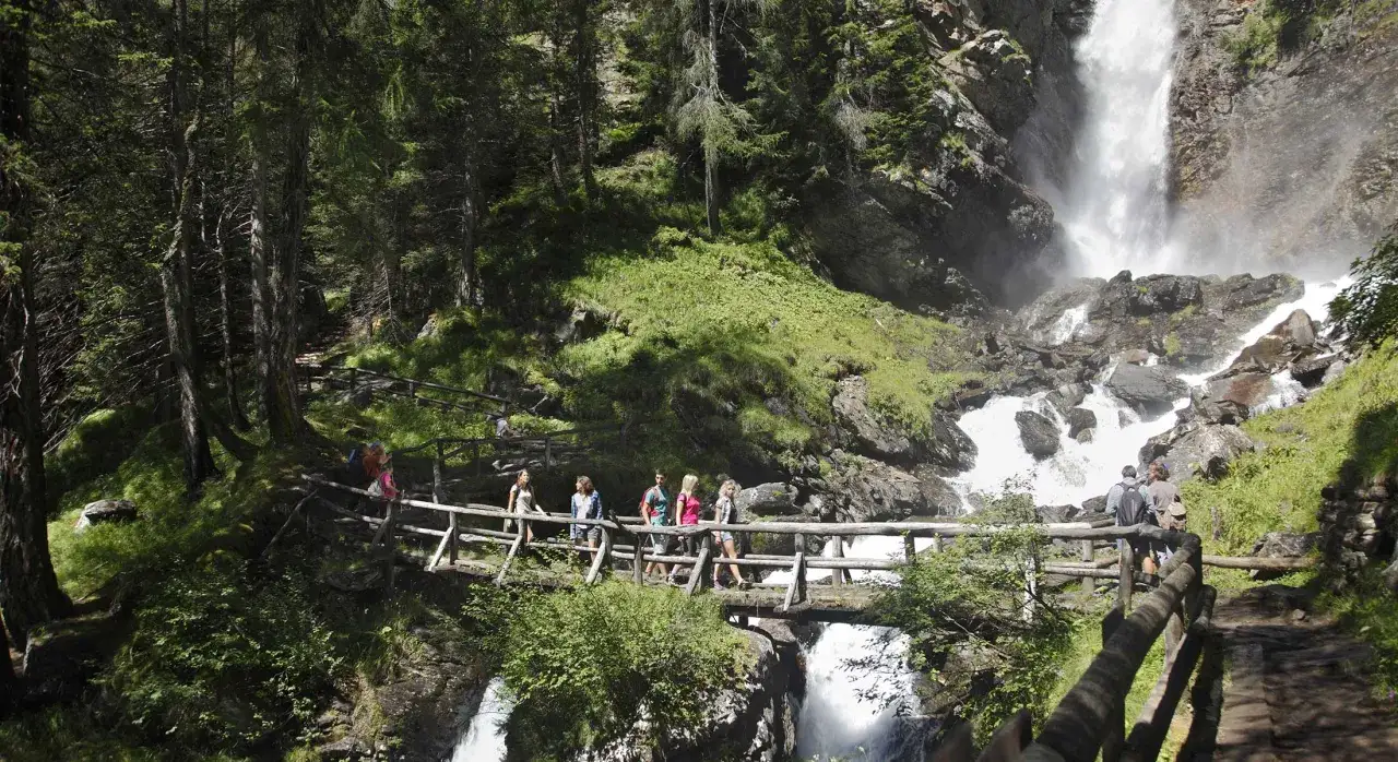 Escursionisti su un ponte di legno ammirano una cascata fragorosa, un'esperienza indimenticabile vicino all'hotel Rabbi.