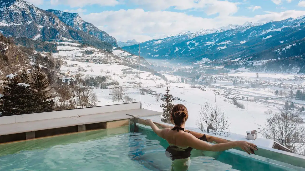 Donna in piscina termale con vista panoramica sulle montagne innevate di Predazzo, un'esperienza indimenticabile all'Hotel La Montanara.