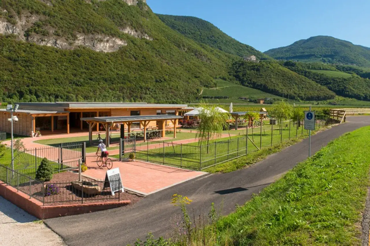 Un ciclista si ferma al bicigrill Faedo, un'oasi di ristoro immersa nel verde, con montagne sullo sfondo.