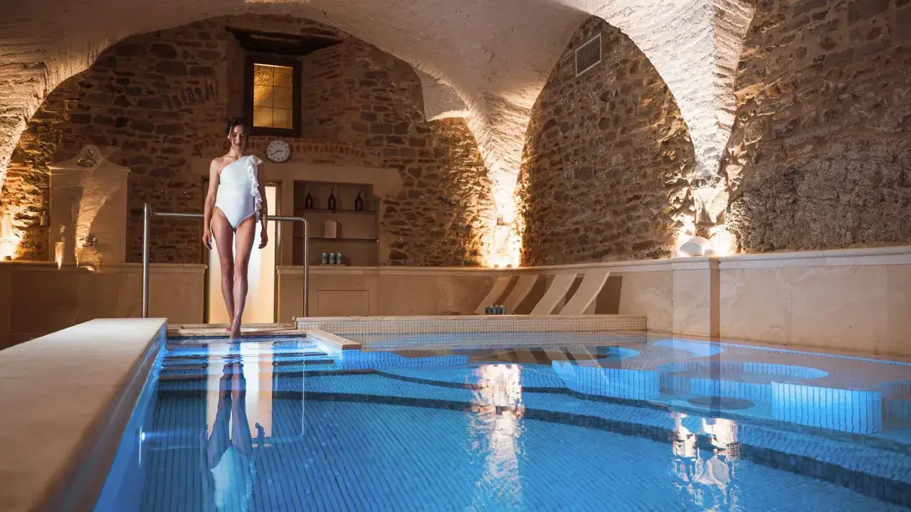 Donna in costume bianco entra in una piscina illuminata da luci blu, un'oasi di relax nel Cortona Resort e Spa.