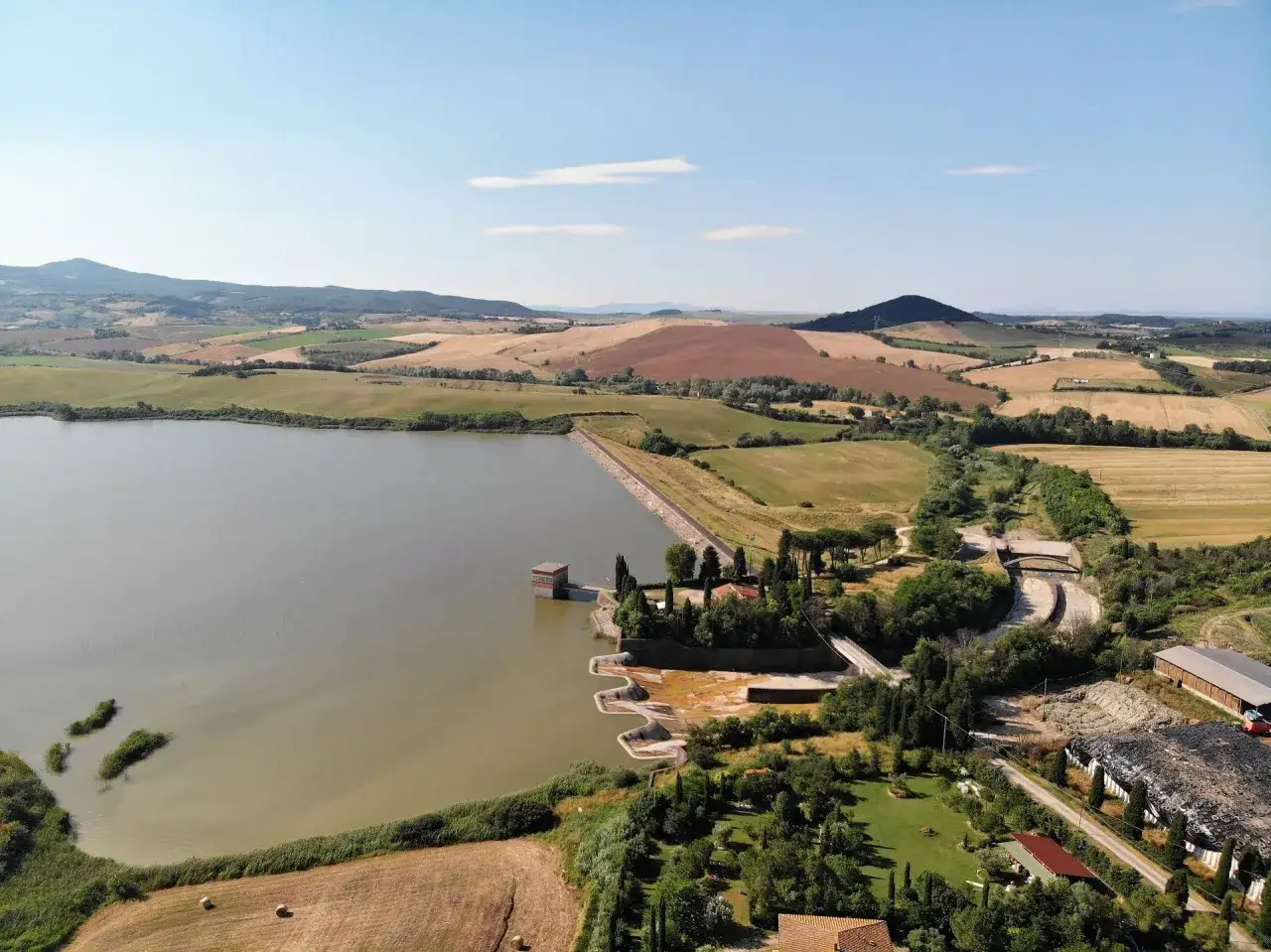 Vasta distesa d'acqua del lago di Santa Luce, circondata da dolci colline toscane coltivate e alberi.