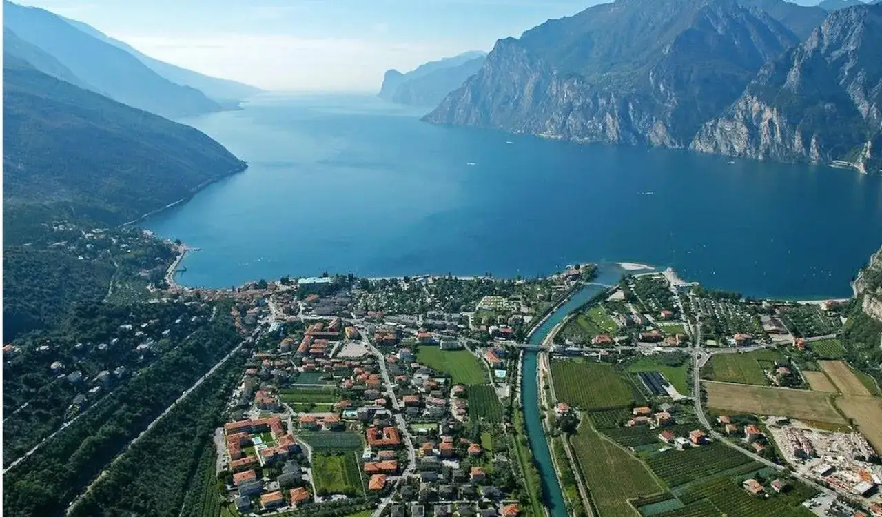 Vista aerea di Torbole sul Garda, con il lago blu intenso e le montagne imponenti. Un luogo ideale per il camping in Europa.