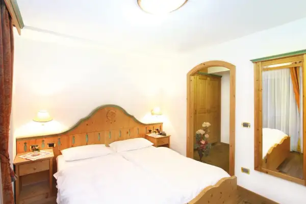 Camera accogliente con letto matrimoniale, arredi in legno e un'apertura verso un armadio. Il tuo soggiorno al hotel Diamant Park sarà rilassante.