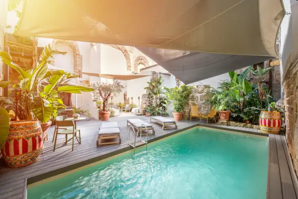 Courtyard pool with lounge chairs, lush plants, and a decorative barrel under a sunshade.