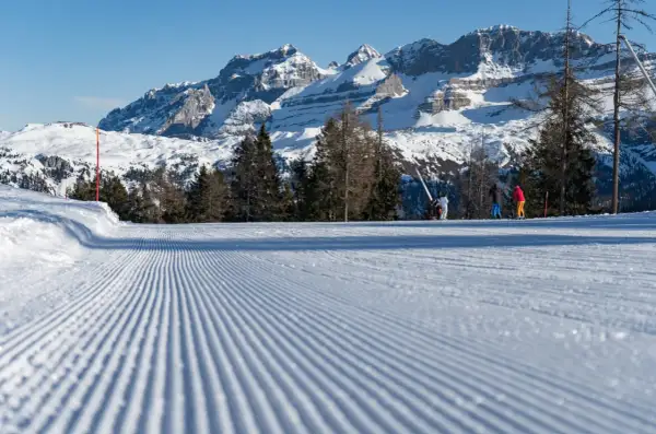 Piste da sci perfettamente battute a Pinzolo, con sciatori sullo sfondo e maestose montagne innevate.