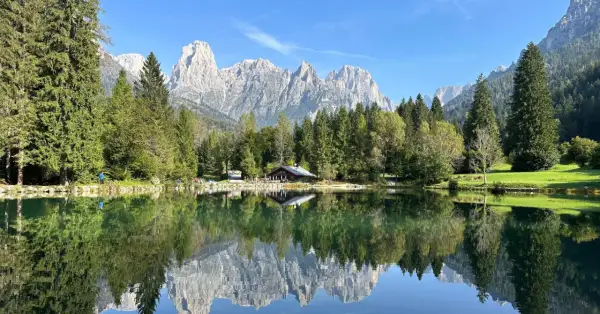 Riflessi perfetti sul lago Welsperg: montagne maestose, boschi verdi e un rifugio alpino.