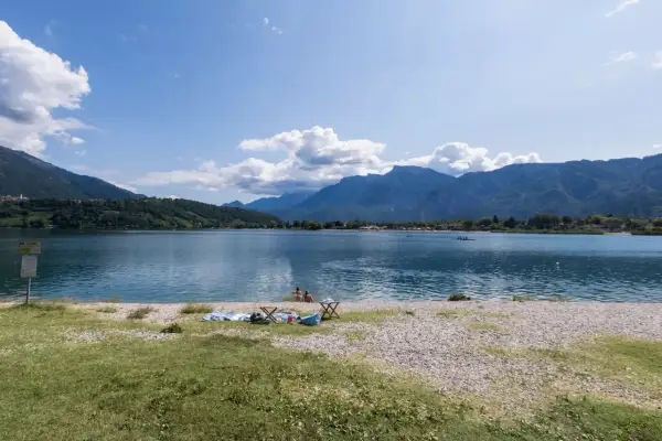 Relaxing day al lido di Caldonazzo, con montagne sullo sfondo e persone che si godono il sole e il lago.