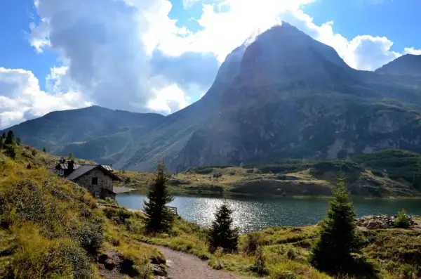 Sentiero che porta al **lago Colbricon**, con un rifugio in pietra e un maestoso monte sullo sfondo.