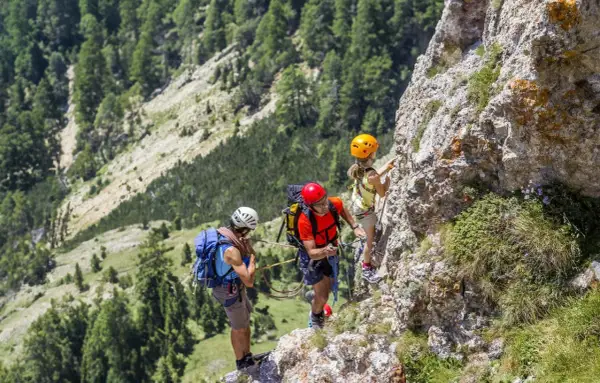 Famiglia in avventura sulle ferrate Dolomiti. Un padre guida la figlia su un sentiero attrezzato, mentre un altro adulto li assicura.