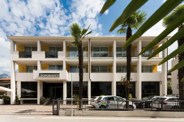 Hotel Gardesana a Riva del Garda, con palme e cielo azzurro. Un'auto bianca parcheggiata davanti.