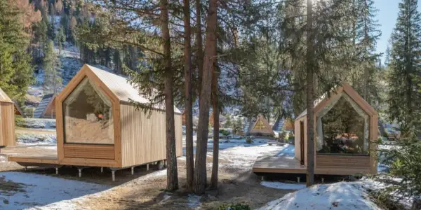 Piccole case in legno con grandi vetrate, immerse in un bosco innevato. Un'oasi di pace per alloggi particolari.