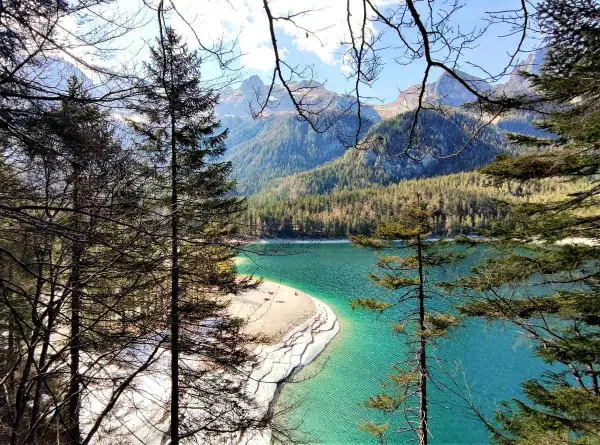Un lago turchese incorniciato da alberi e montagne nel Val di Non. La spiaggia sabbiosa invita a una sosta.