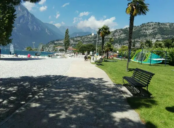 Vacanze in campeggio Europa a Torbole: spiaggia con windsurf, montagne sullo sfondo e area giochi per bambini.