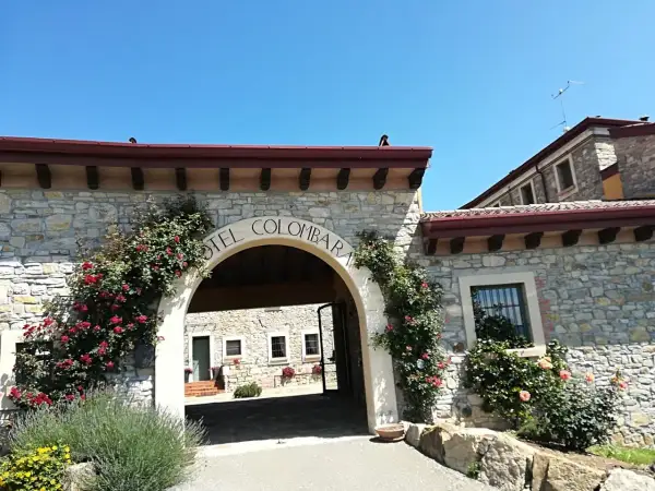 Ingresso in pietra del relais La Colombara, con rose rosse rampicanti e un arco che porta a un cortile interno.