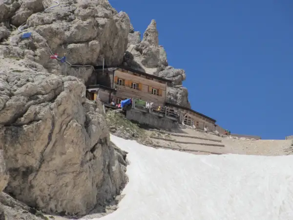 Rifugio Passo Principe, un rifugio alpino in legno incastonato tra rocce imponenti e neve, con un cielo azzurro limpido.