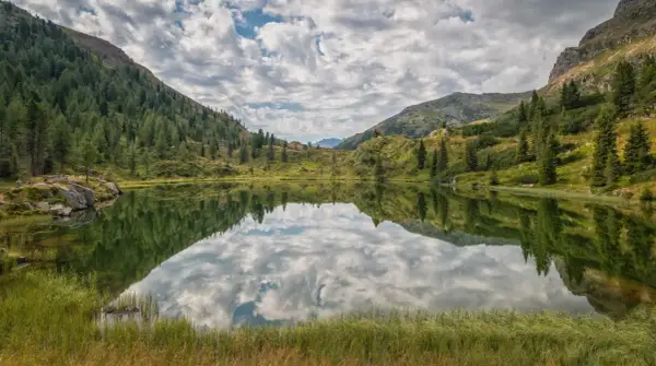 Lago alpino con riflessi di montagne e cielo nuvoloso, un'oasi di pace in una splendida cavalese estate.