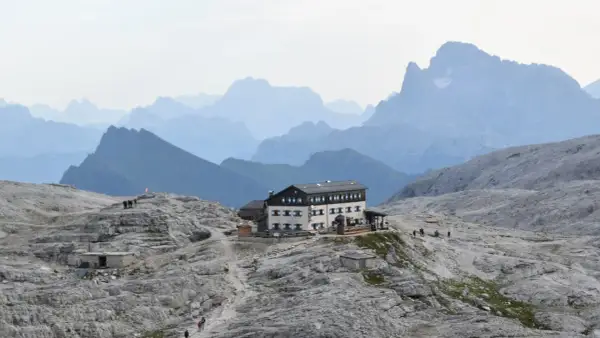 Il rifugio Rosetta, un edificio imponente, si erge su un terreno roccioso con montagne sfumate all'orizzonte.