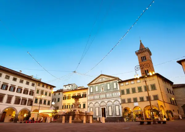 Piazza di Empoli illuminata da luci natalizie, con la fontana, la chiesa e il campanile che si stagliano sotto un cielo azzurro.