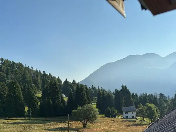 Un casolare bianco, forse la locanda La Ruscoletta, immerso nel verde di un prato e circondato da alberi, con montagne nebbiose sullo sfondo.