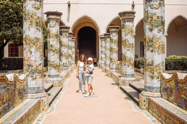 Un madre e figlio passeggiano tra colonne decorate con maioliche, un luogo incantevole tra i tanti posti da visitare a Napoli.