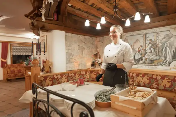 Chef sorridente in un accogliente hotel senza glutine in Trentino, con un buffet di dolci e piatti pronti.