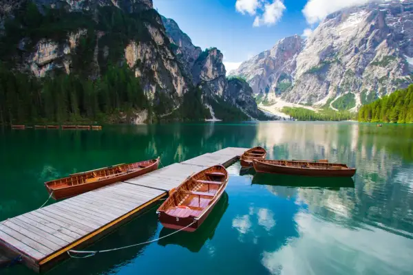 Barche di legno ormeggiate su un pontile in un lago alpino, circondato da montagne imponenti e foreste verdi. Un paesaggio da sogno tra i laghi trentino.
