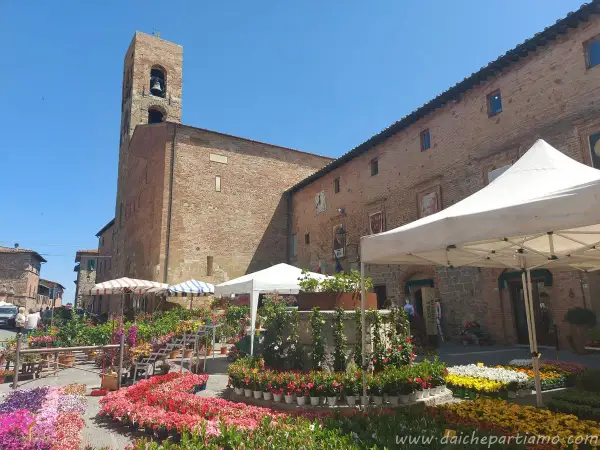 Mercato fiorito a Casole d'Elsa, con bancarelle colorate e un'antica torre campanaria sullo sfondo.