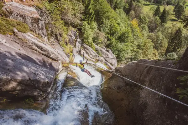 Donna in zipline sopra una cascata nella Val Daone, con rocce e alberi circostanti.