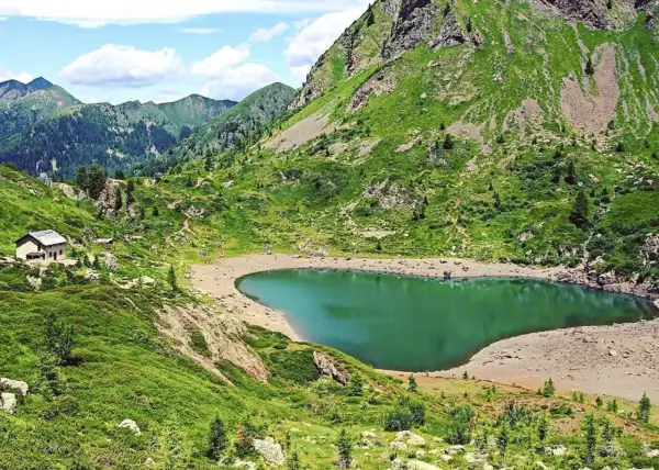 Un rifugio solitario vicino al **lago di Erdemolo**, circondato da verdi pendii montuosi e un cielo azzurro con nuvole bianche.