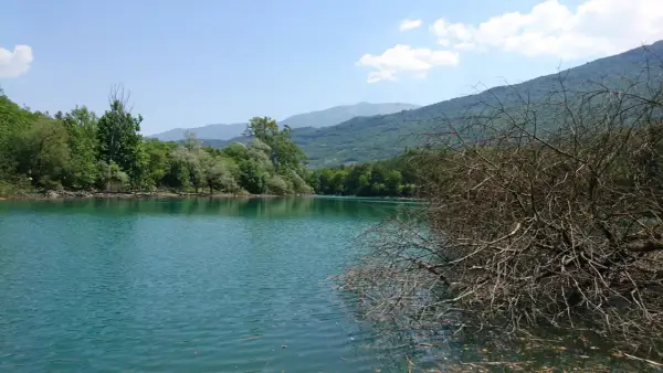 Acque turchesi del lago di Cavedine circondato da rigogliosa vegetazione e montagne sullo sfondo.