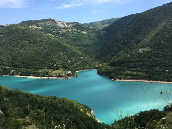 Splendido lago di Fiastra con acque turchesi, incastonato tra verdi colline boscose sotto un cielo azzurro.