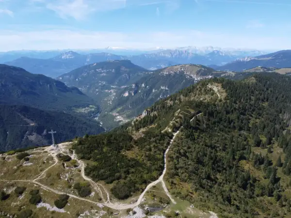 Sentiero che sale verso la croce sul monte Maggio, con vista su valli verdi e montagne all'orizzonte.