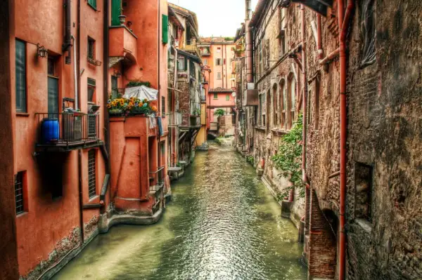 Un canale con edifici color ocra e mattoni, un assaggio di cosa vedere a Bologna, con fiori su un balcone.