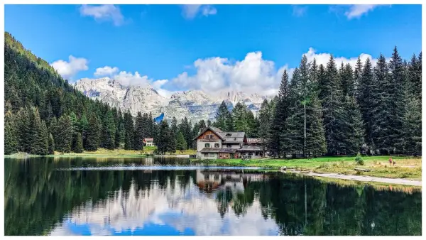 Riflessi sull'acqua del lago Nambino, con un rifugio alpino e montagne sullo sfondo.