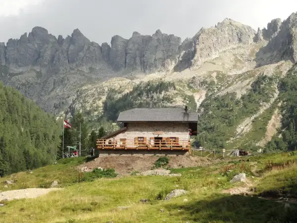 Il rifugio Caldenave, un'accogliente baita in pietra, si erge su un prato verde ai piedi di imponenti montagne rocciose.