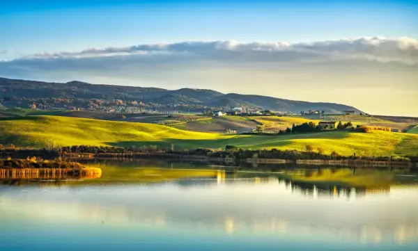 Dolci colline toscane illuminate dal sole al tramonto si specchiano nel lago di Santa Luce, creando un paesaggio incantevole.
