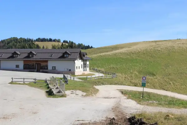 Malga Arpaco, un edificio bianco con tetto scuro, si erge su un prato verde sotto un cielo azzurro.