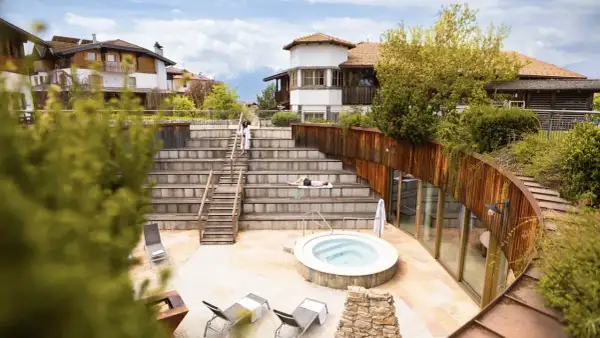 Relaxing at Pineta Nature Resort: un uomo prende il sole su una scalinata in legno, vicino a una vasca idromassaggio e a un edificio moderno.